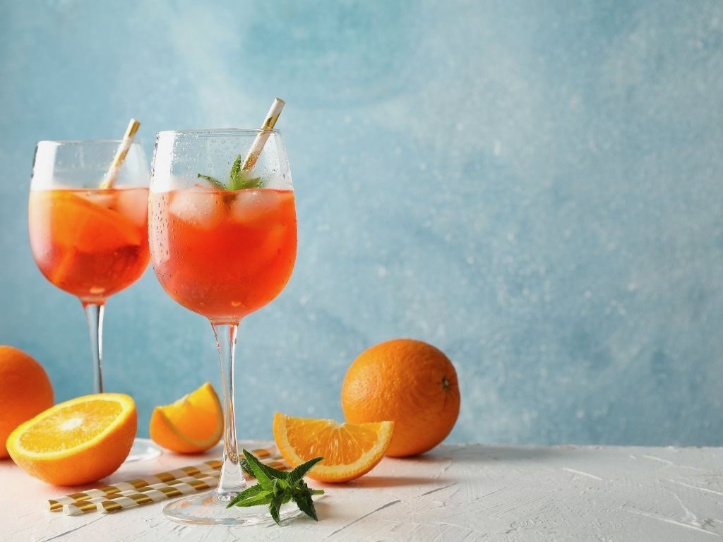 Two glasses of orange aperol sprit against a blue background