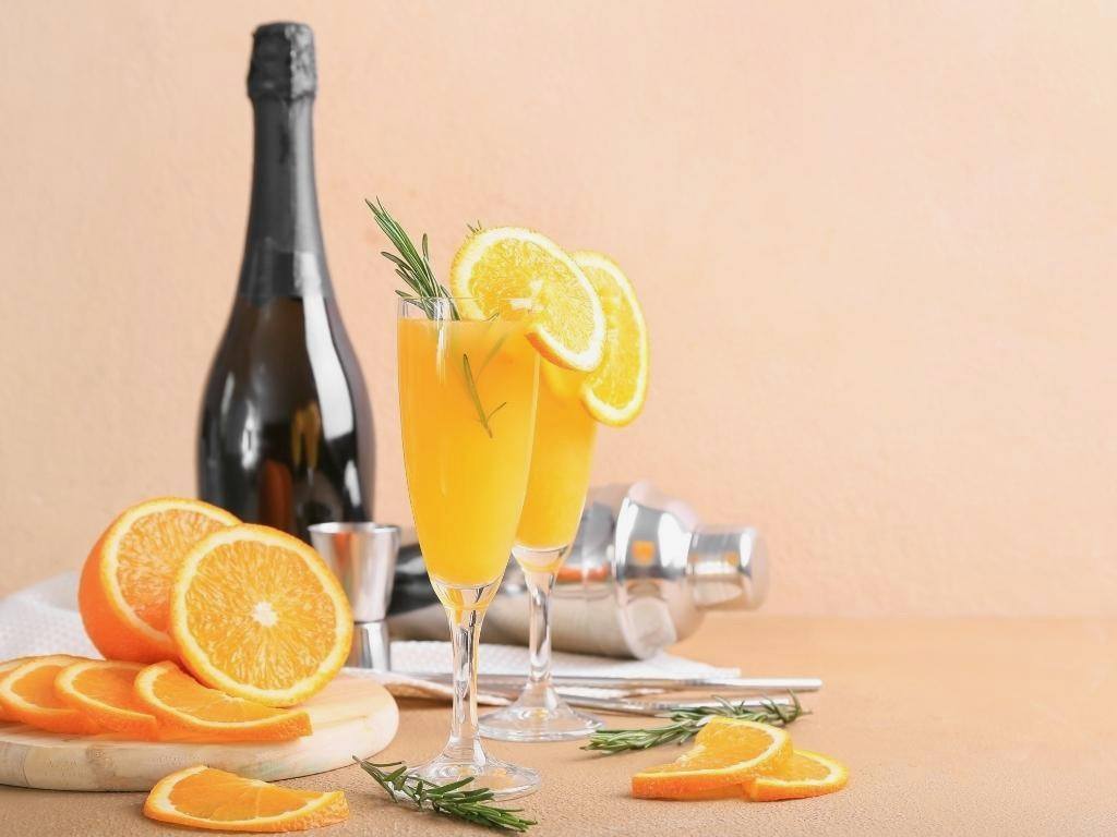 Champagne bottle, sliced oranges and flutes with mimosa cocktail